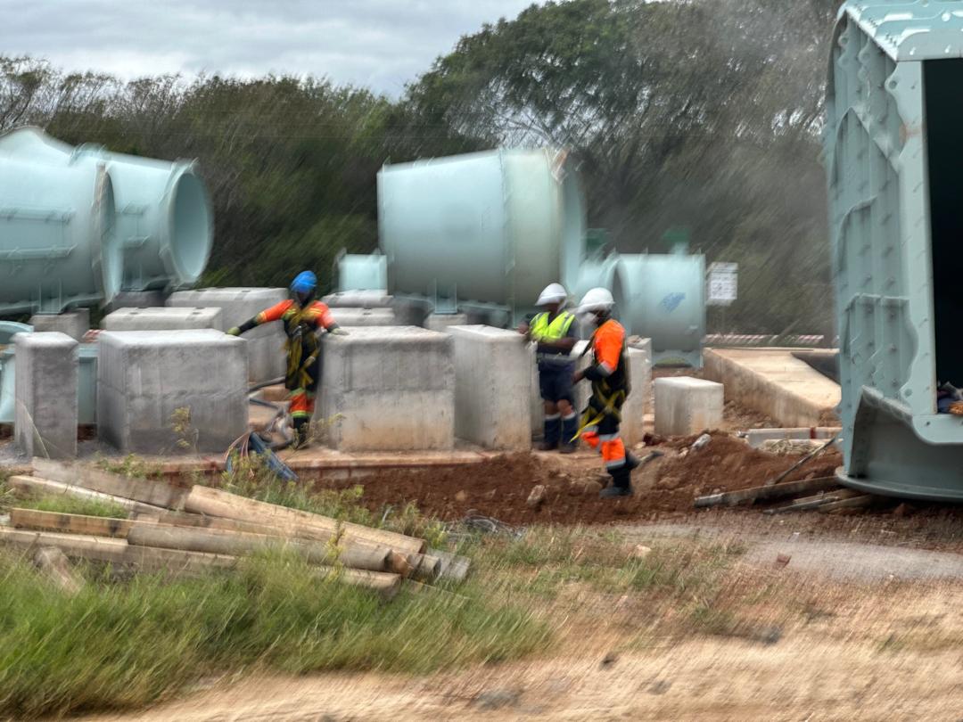 Site staging — workers at concrete plinths between fan units (N7)